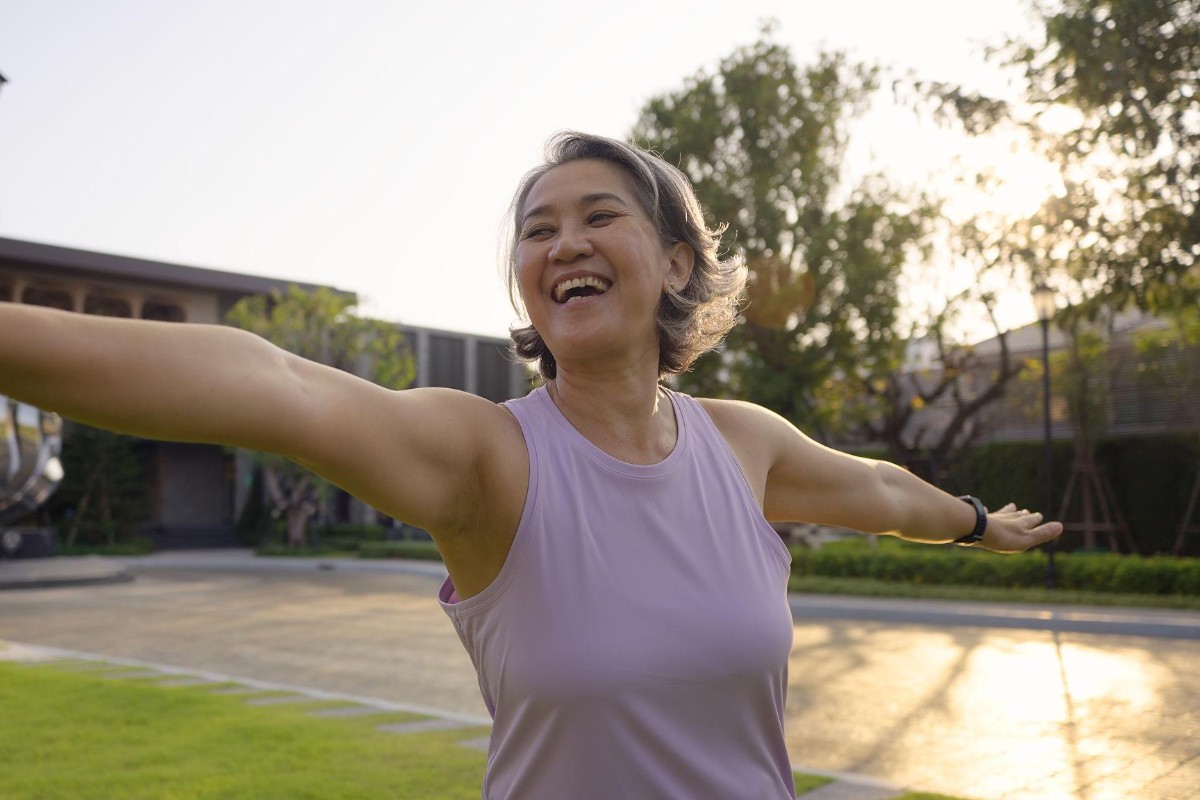 Woman with arms open, smiling in a park at sunrise